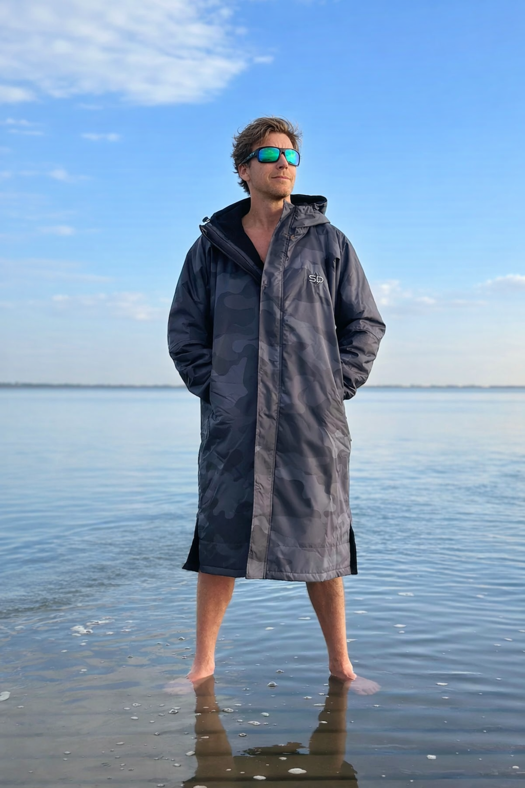 Person wearing a changing robe standing on a beach with clear blue sky.