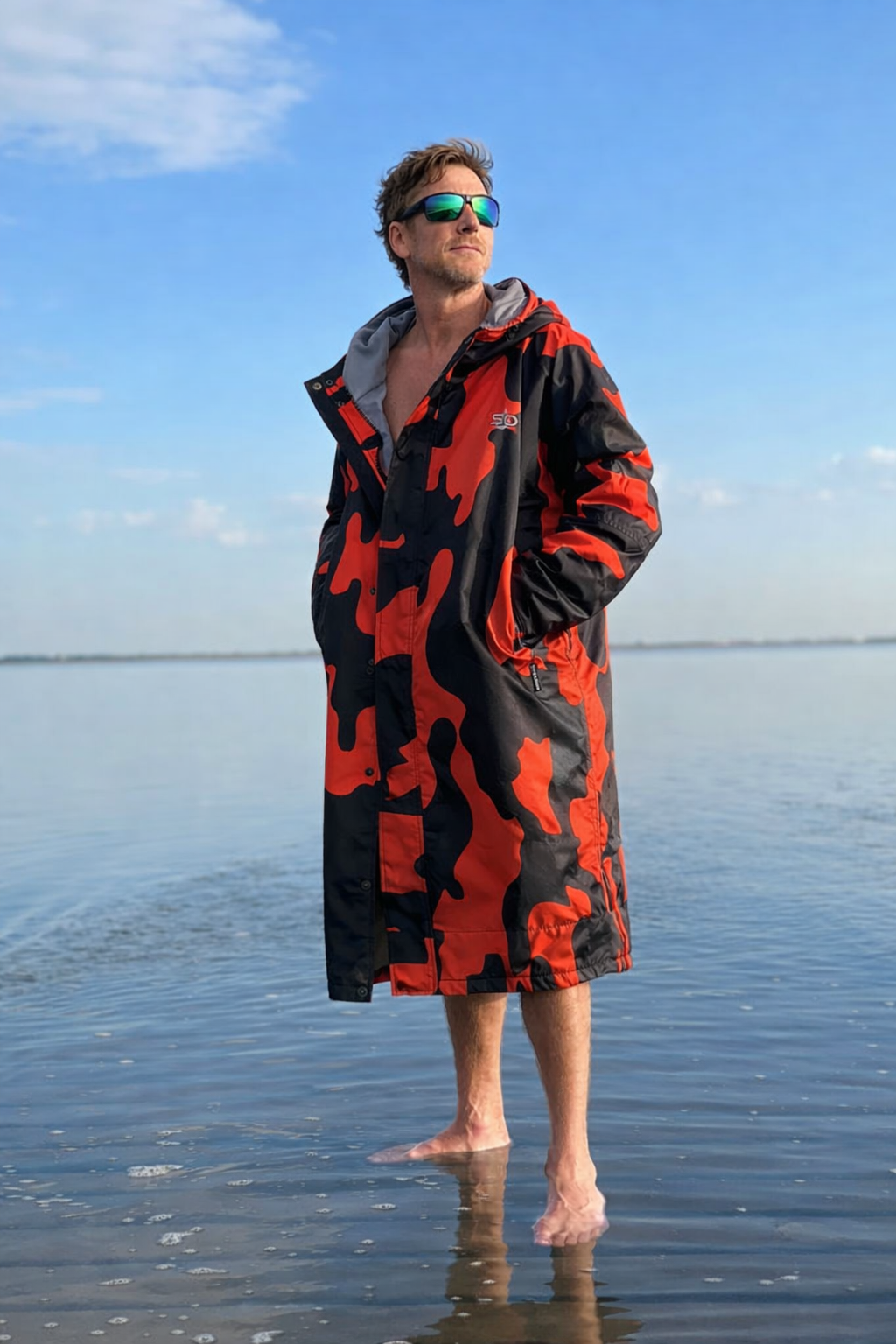 Man wearing an orange and black camouflage robe standing on a beach.