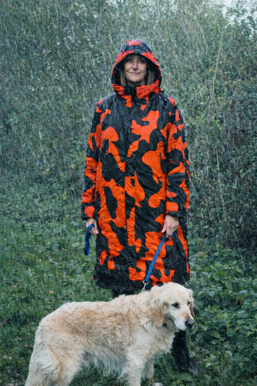 Person wearing an and black patterned raincoat with a dog in the rain.range