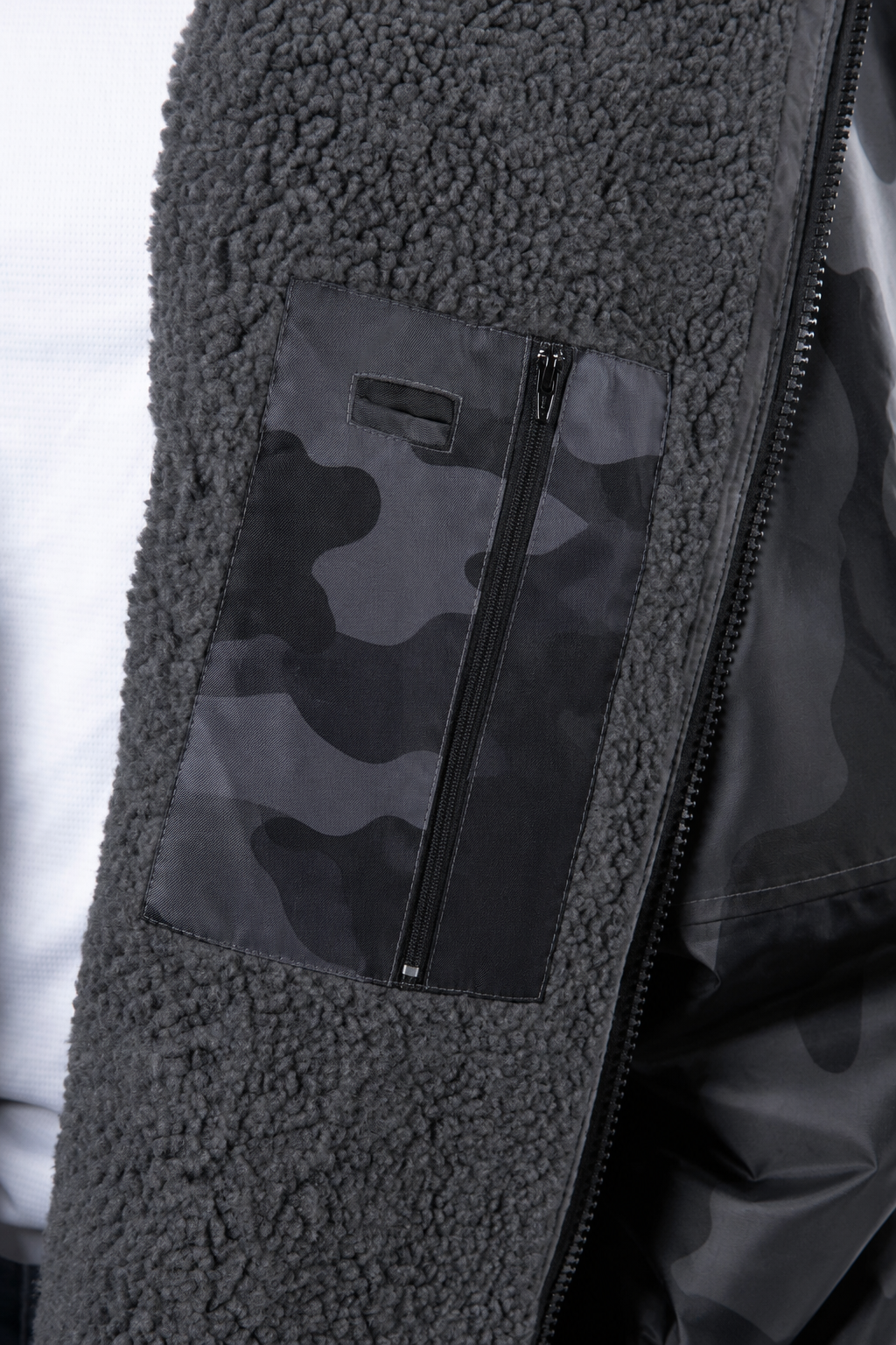 Close-up of a dark gray fleece jacket with a black and gray camouflage zippered  inside phone pocket 